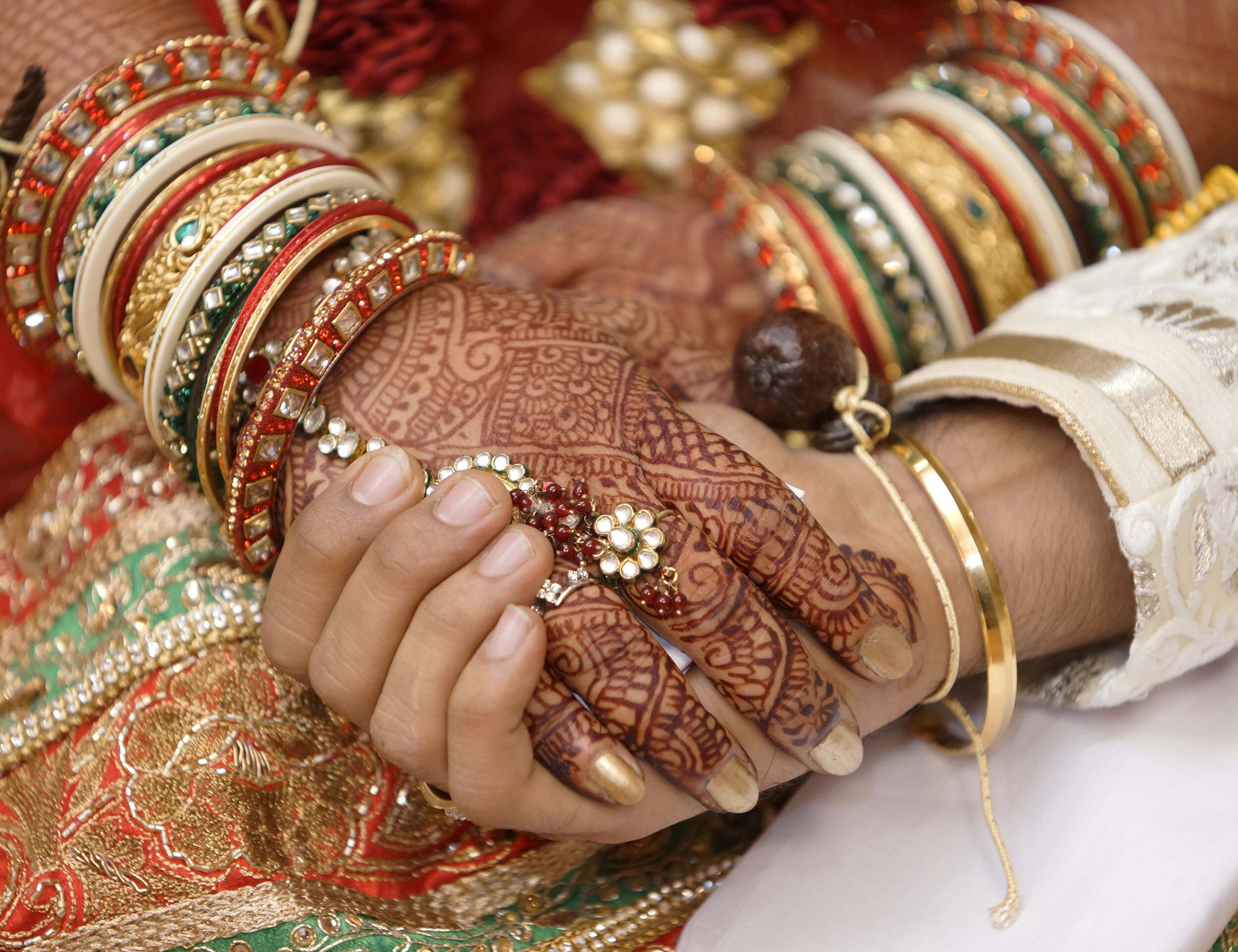 A bride gently placing her beautifully decorated mehendi hand on the groom’s hand, symbolizing love and togetherness